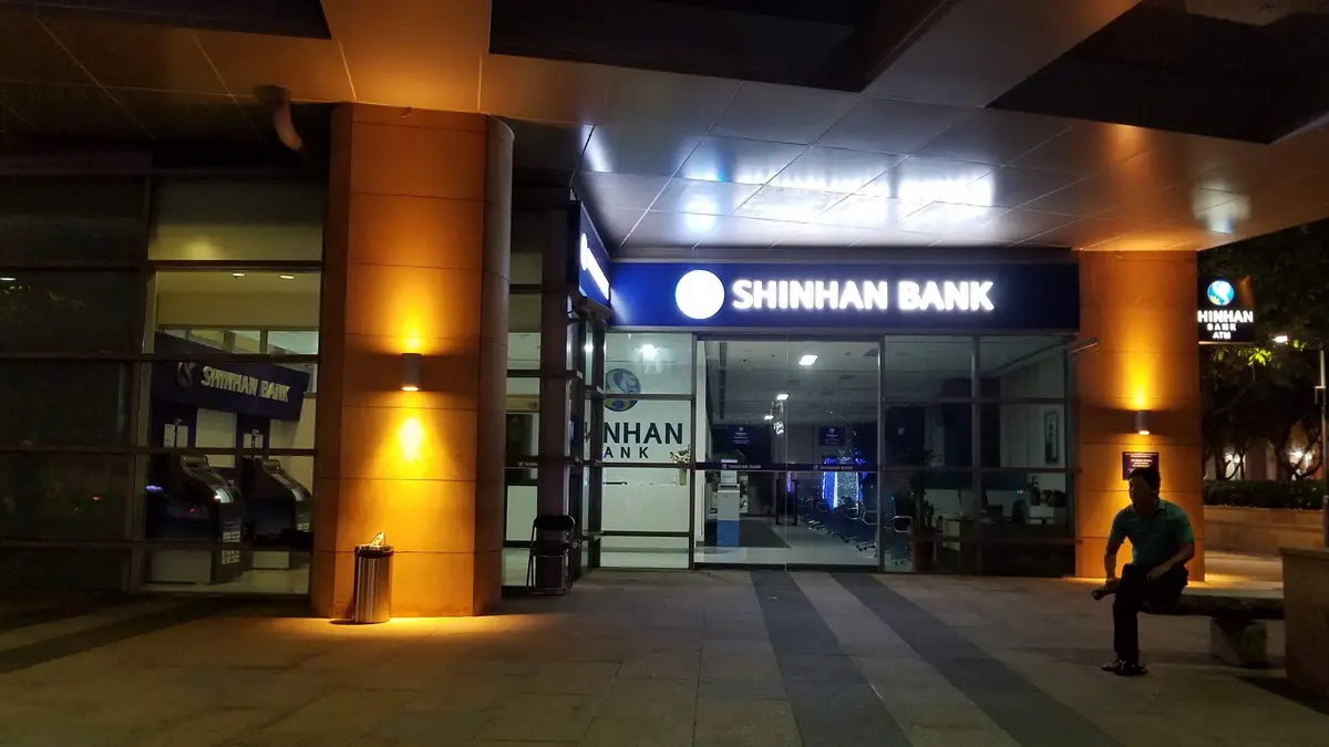 Lit Shinhan Bank glass entrance at dusk with warm wall lights.