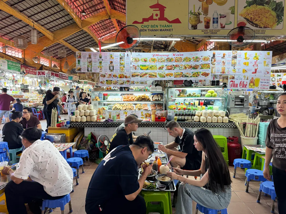 Customers eating at small tables beside food stalls in a covered market hall