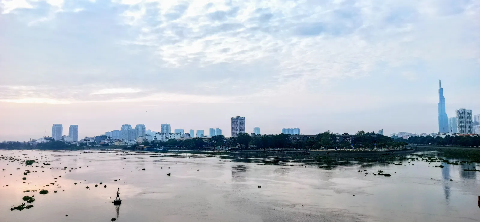 Wide grey river with low banks and a distant city skyline under a pale sky