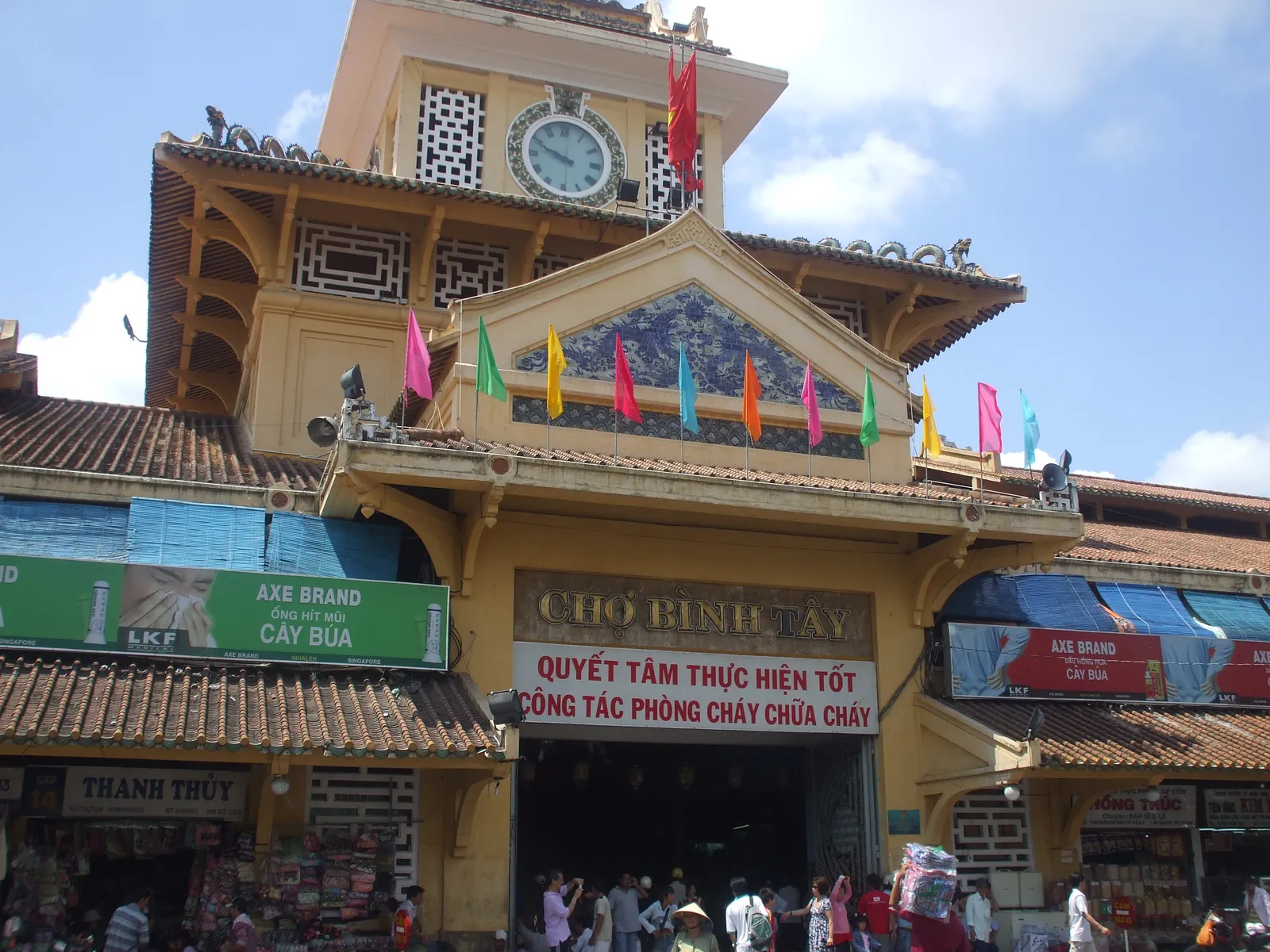 Yellow market gatehouse with a clock tower, flags and a Cho Binh Tay sign above the entrance