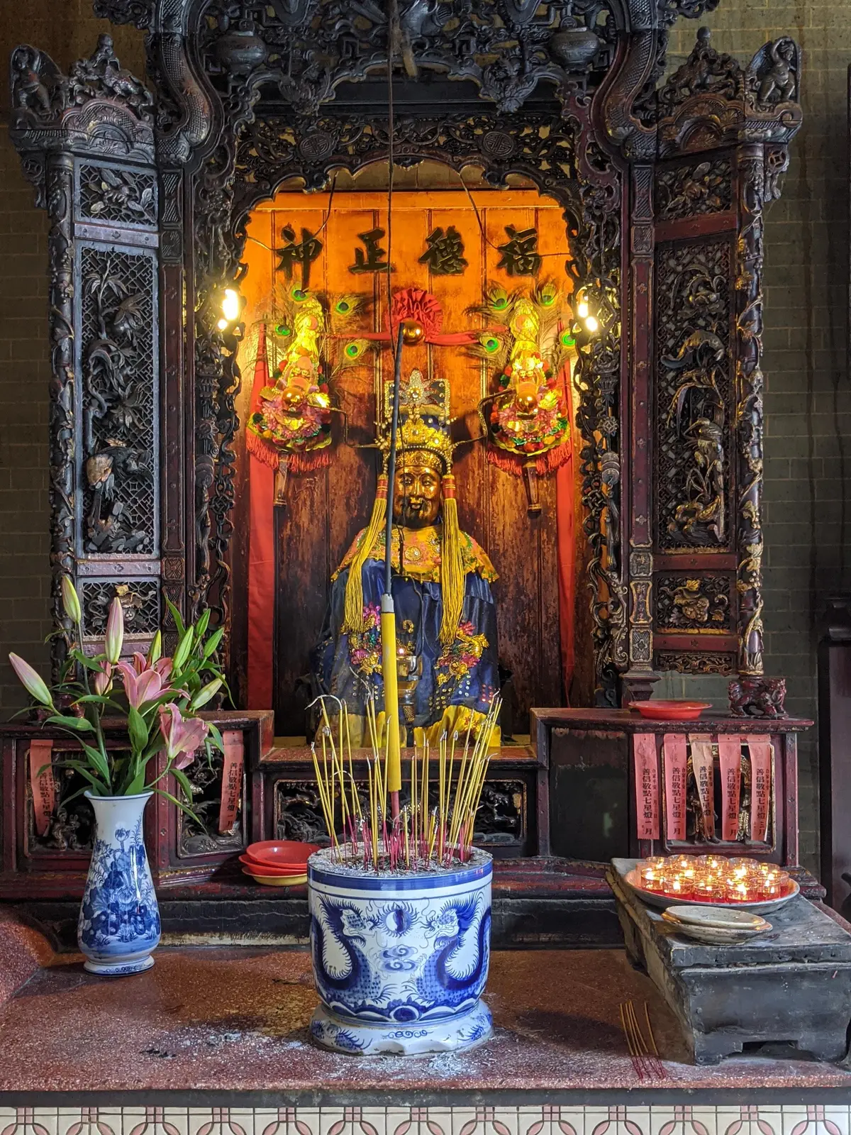 Gilded statue of the sea goddess behind a bowl of burning incense sticks in a carved altar