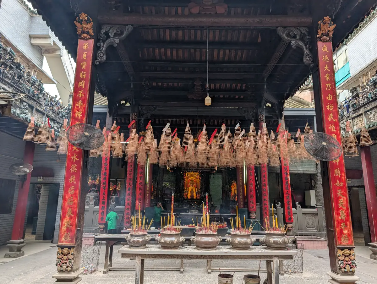 Open temple courtyard with red pillars and rows of hanging incense coils above offering tables