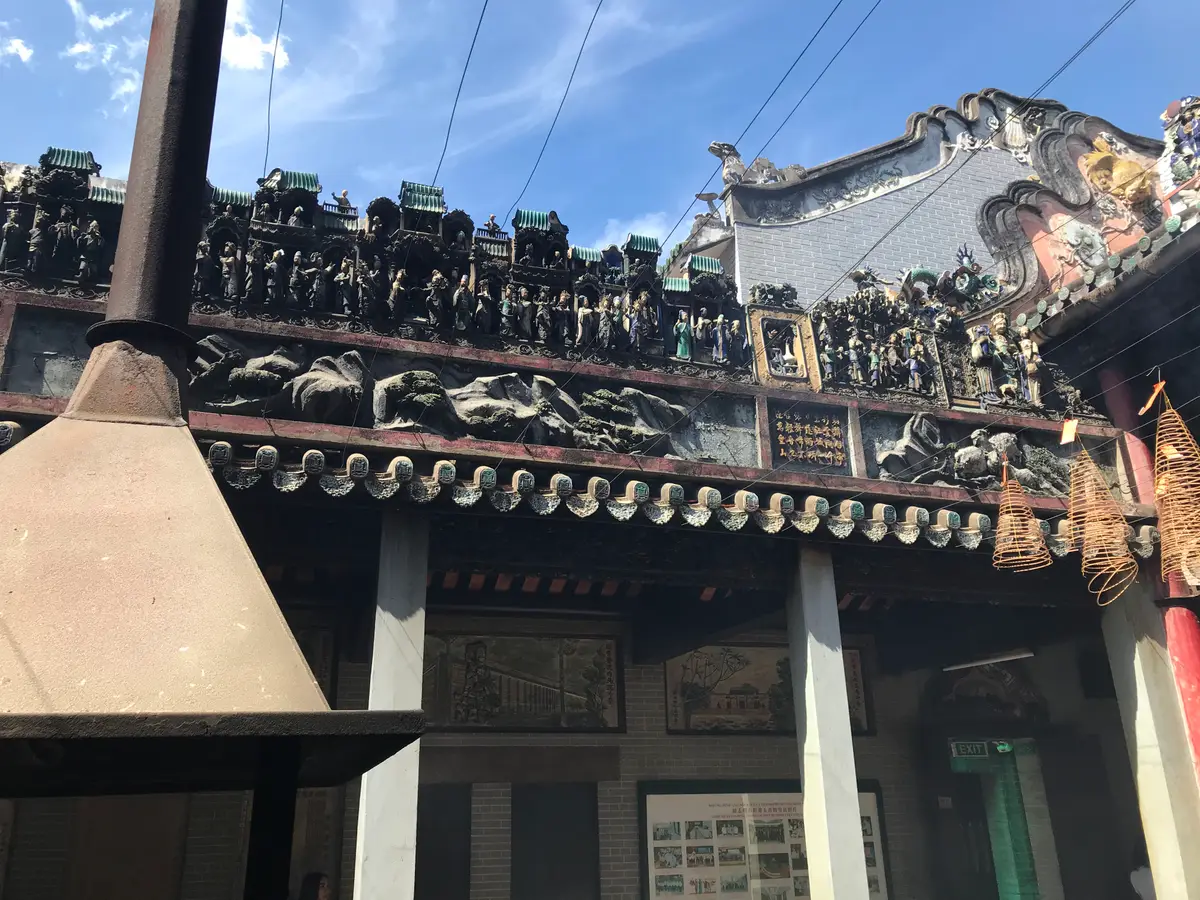 Temple roofline covered in small ceramic figures, with an incense coil in the foreground