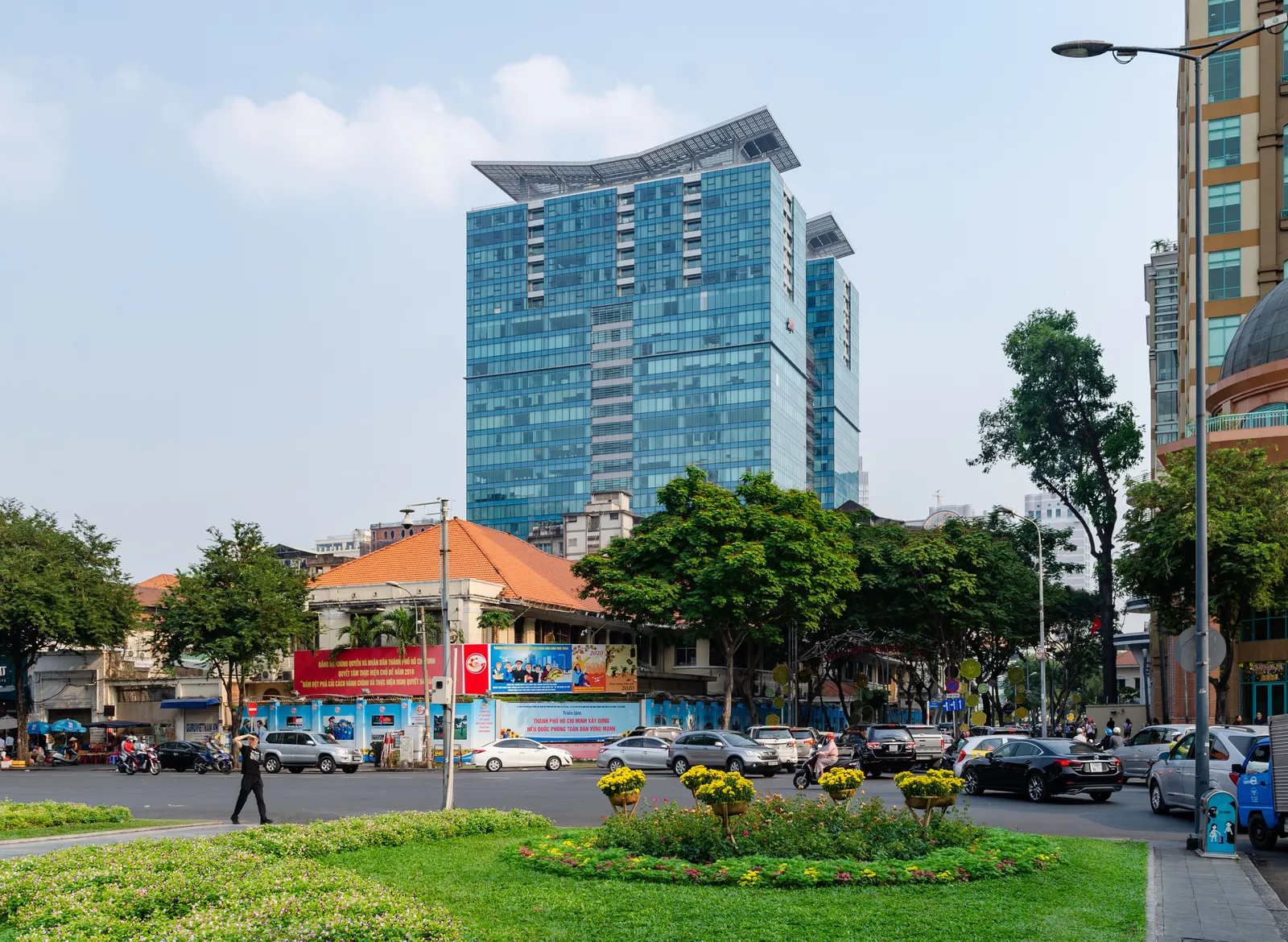 Blue glass tower of Vincom Center behind a green roundabout and traffic in central Saigon