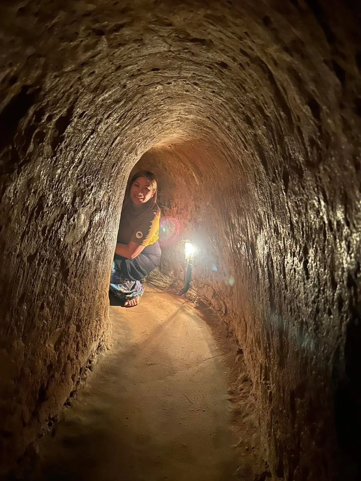 Narrow earth tunnel lit by a torch with a visitor crouching inside