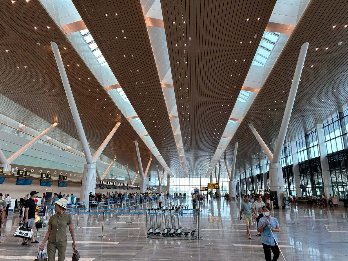 Wide terminal hall at Tan Son Nhat International Airport with a high ceiling, white columns and a few travellers with luggage trolleys.