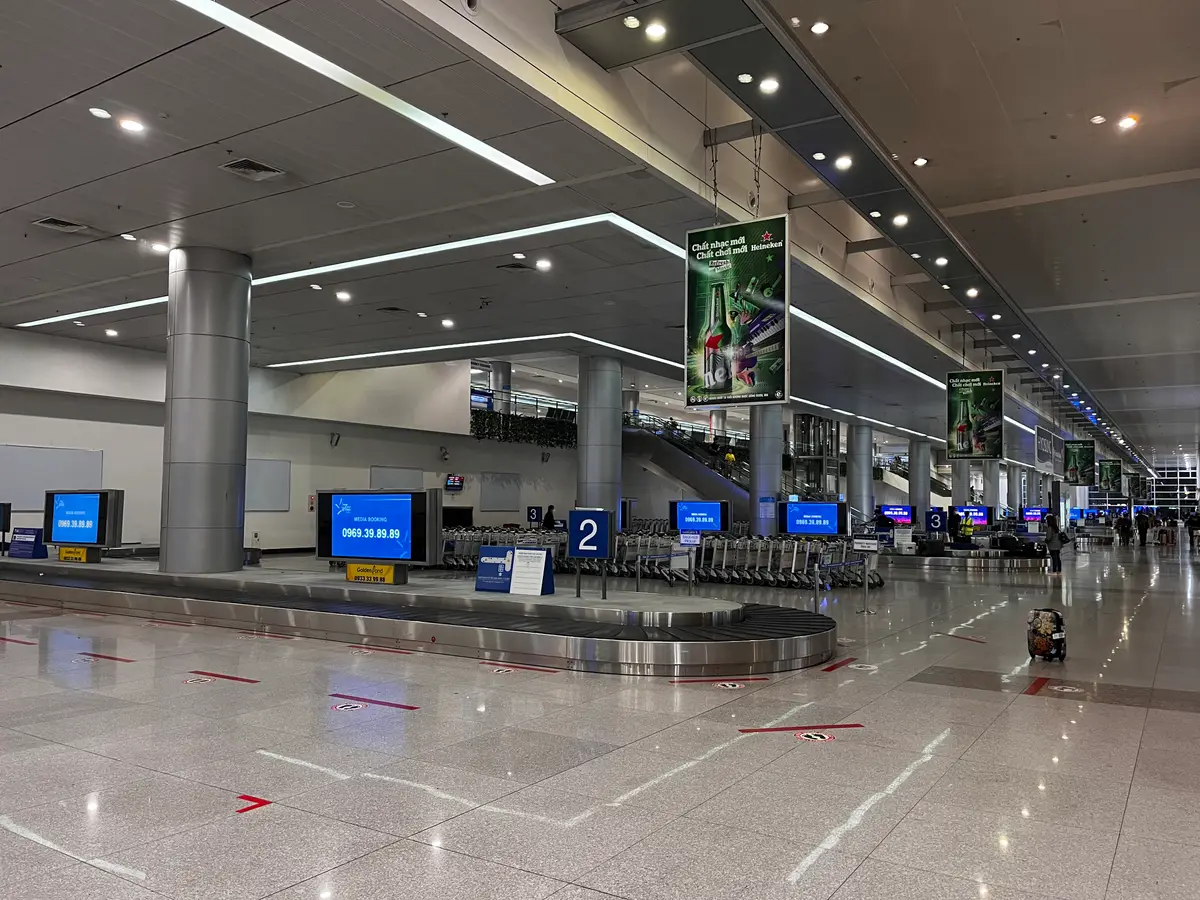 Baggage claim hall at Tan Son Nhat International Airport with carousels, overhead screens and signs.