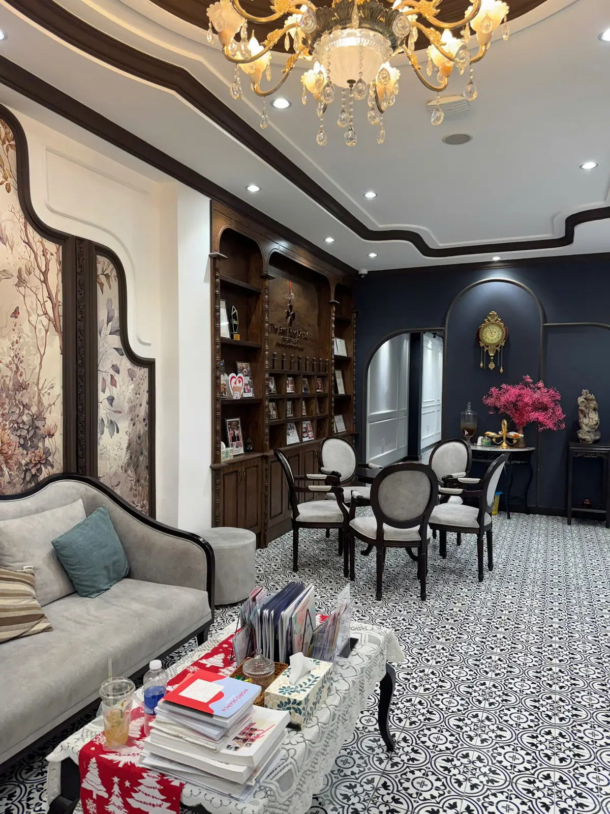 Waiting lounge with a grey sofa, round chairs and dark wood shelves in an ornate classic style.