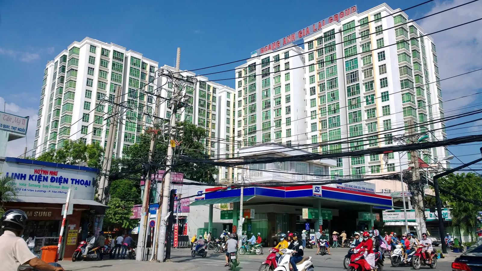 Green and white apartment blocks above a busy street with motorbikes and shopfronts