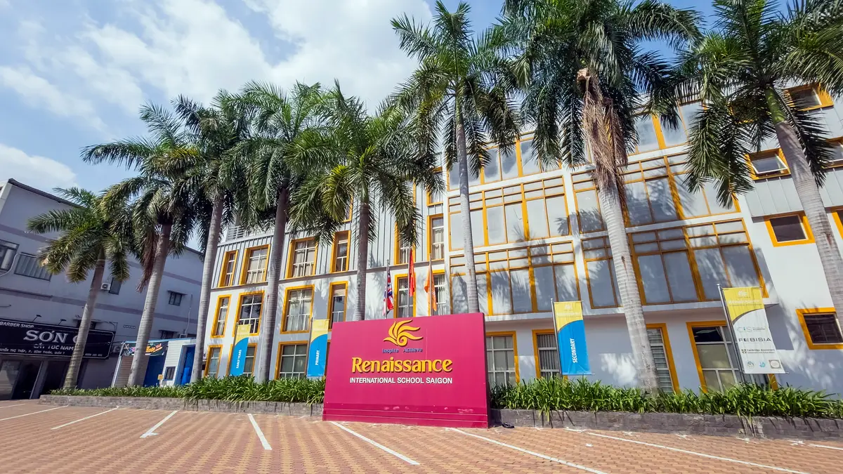 Yellow school building behind palm trees with a red school sign in front