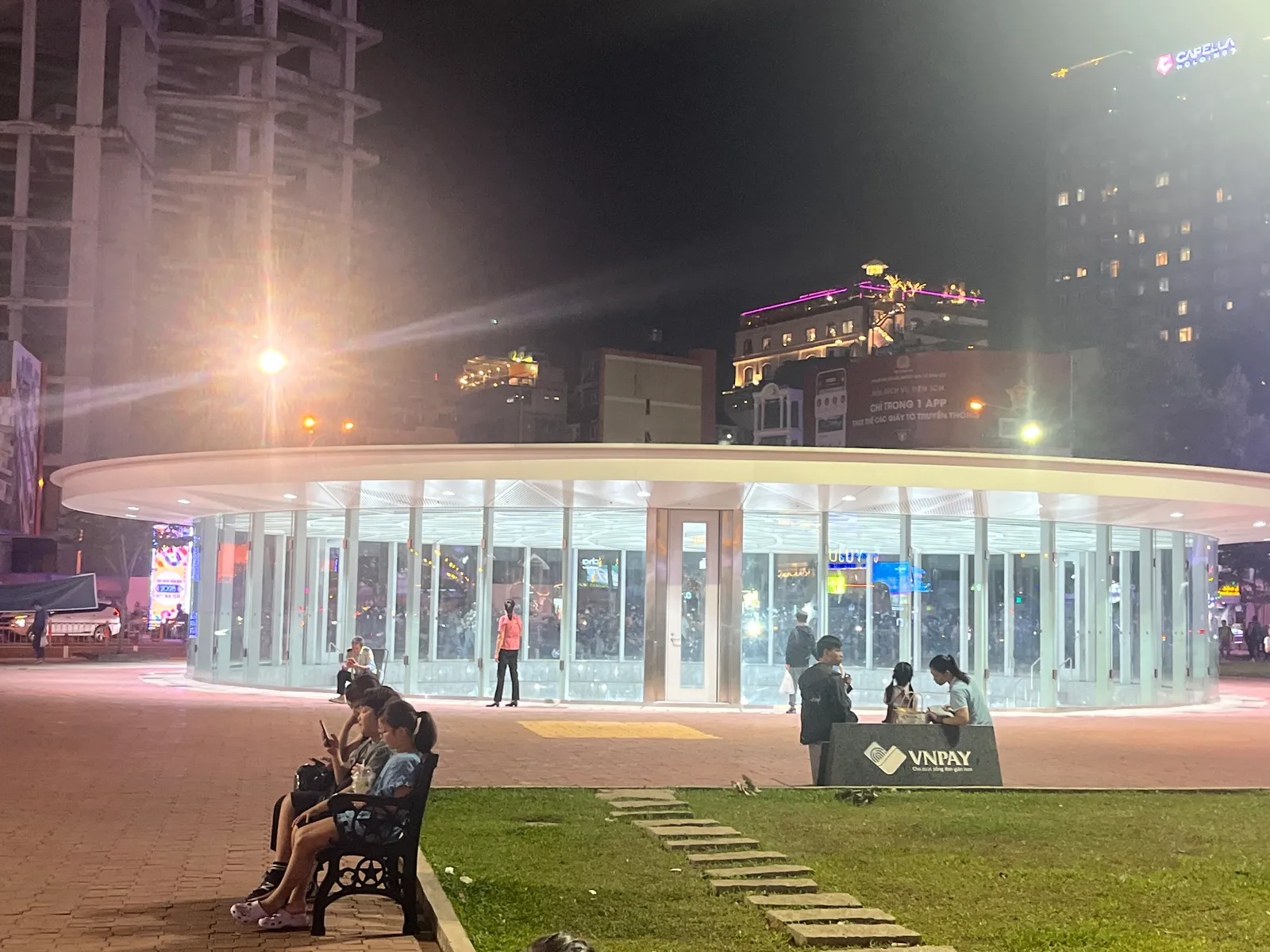 Glass-roofed metro station entrance lit at night beside a small park