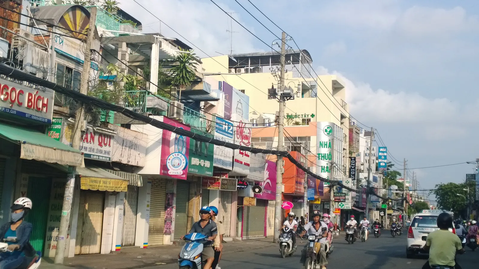Busy street of narrow shophouses with colourful signs and motorbikes under a blue sky