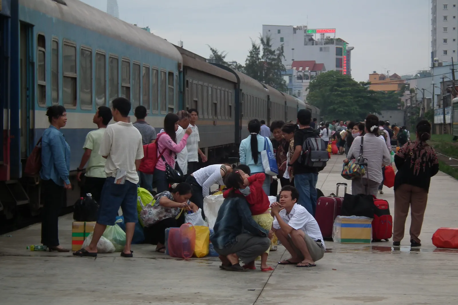 Passengers with luggage waiting on a platform beside a blue train