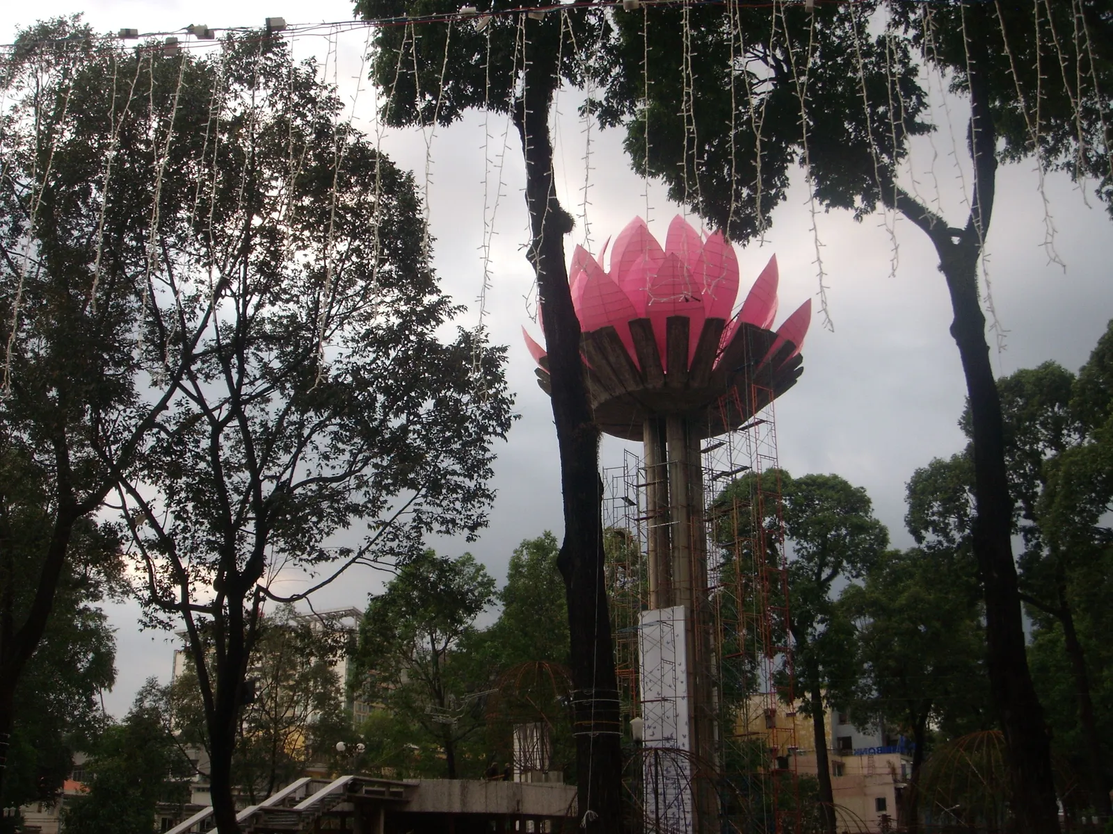 Pink lotus-shaped tower rising above bare trees at a roundabout with string lights