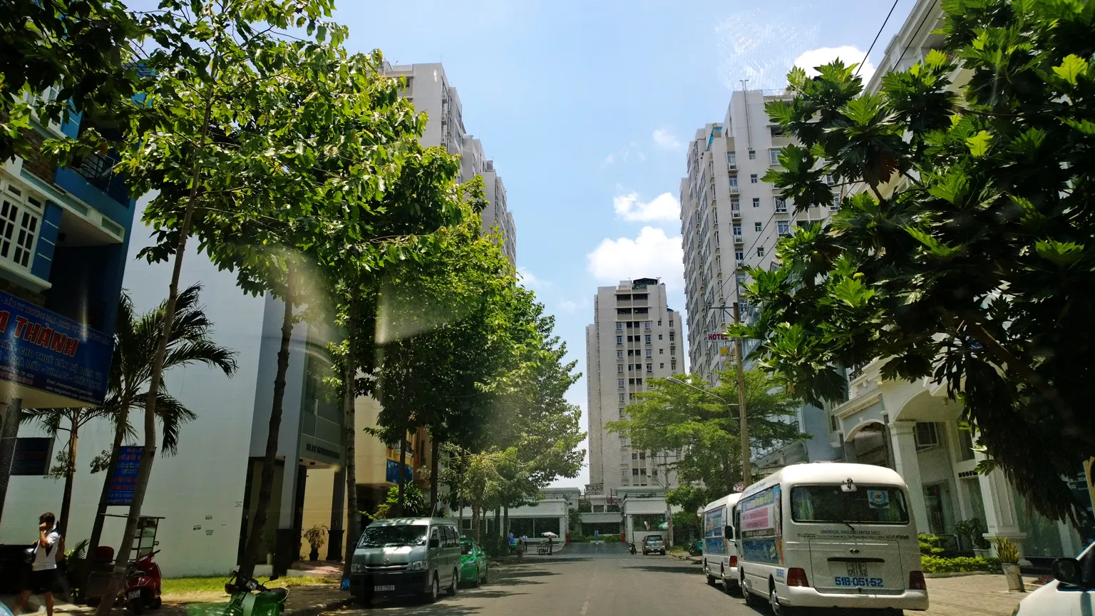 Tree-lined street with a minibus, townhouses and apartment towers in the distance