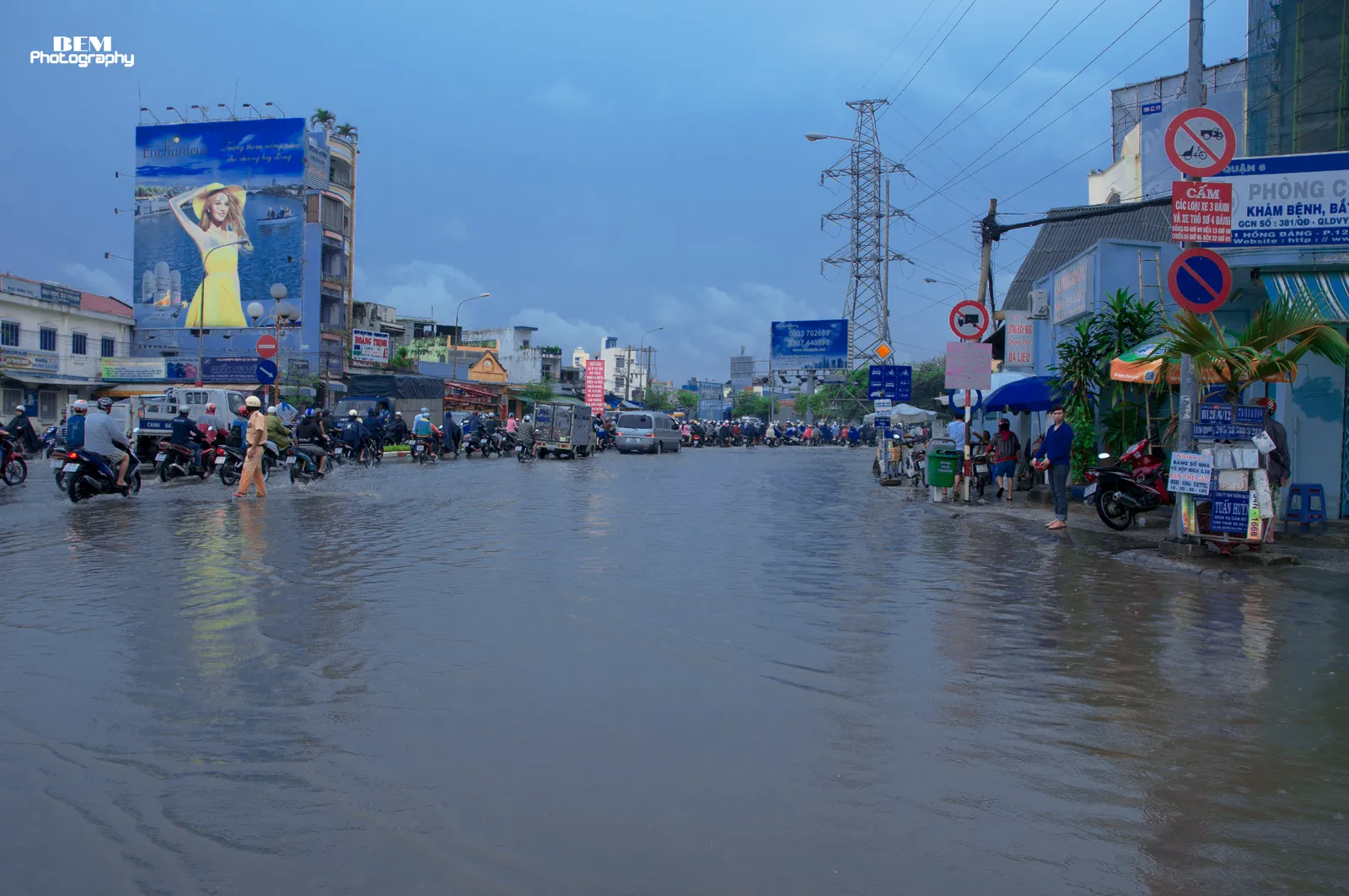 Wide road covered in still water with shops and a billboard beside it