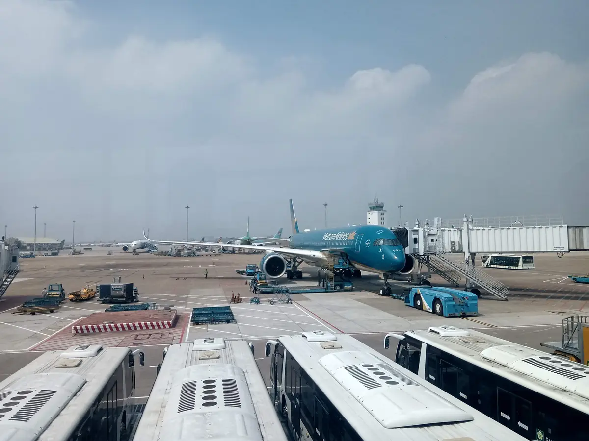 Parked aircraft and white apron buses on an airfield under a hazy sky