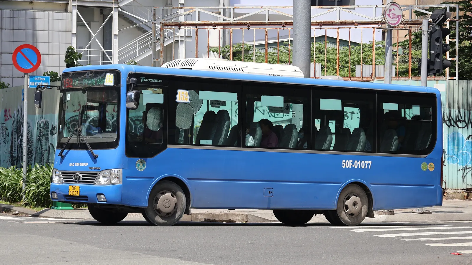Blue city bus with tinted windows on a street corner beside a no-parking sign