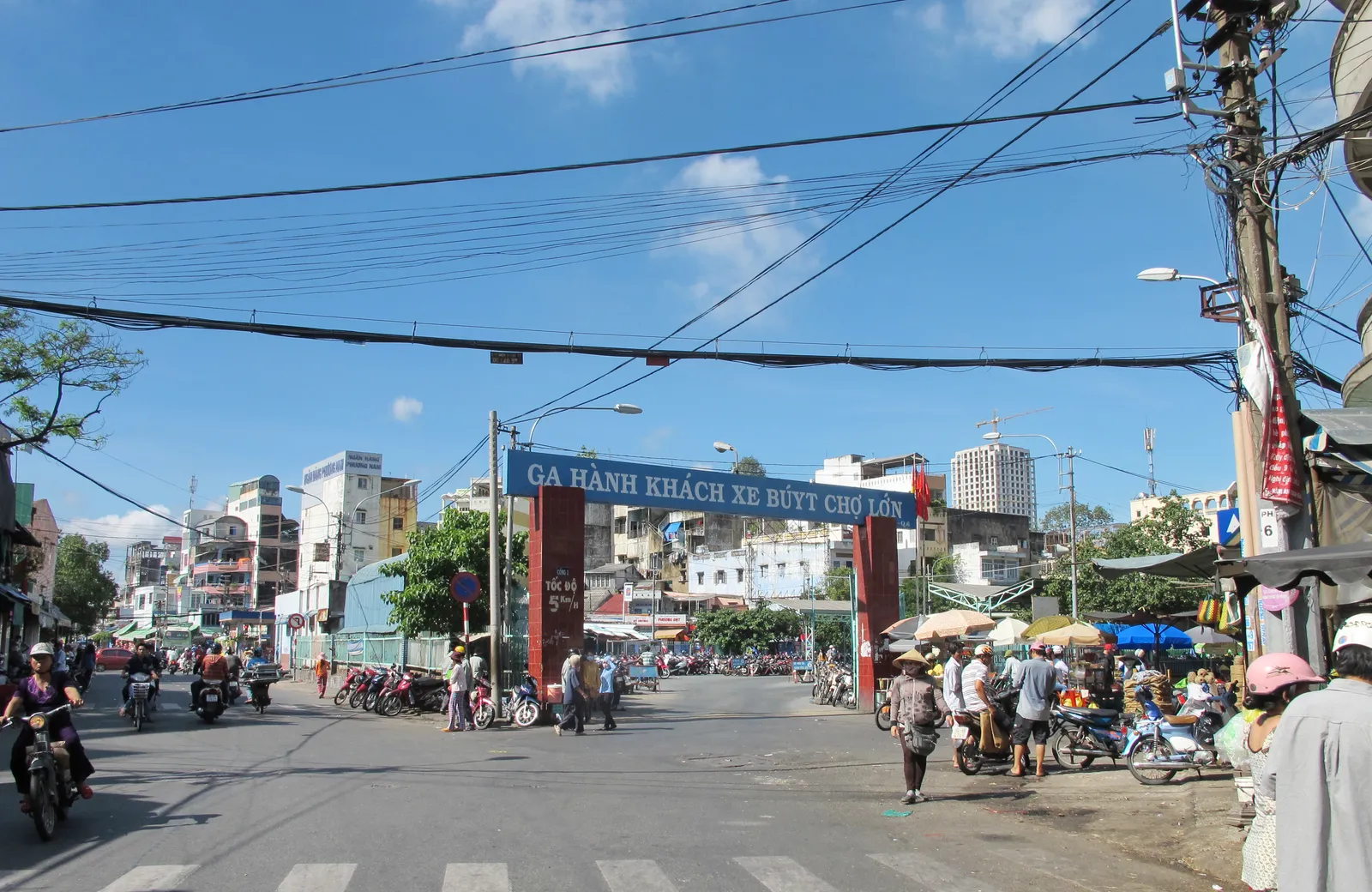 Street with an arch over the entrance of a bus station sign, power lines and apartment blocks beyond
