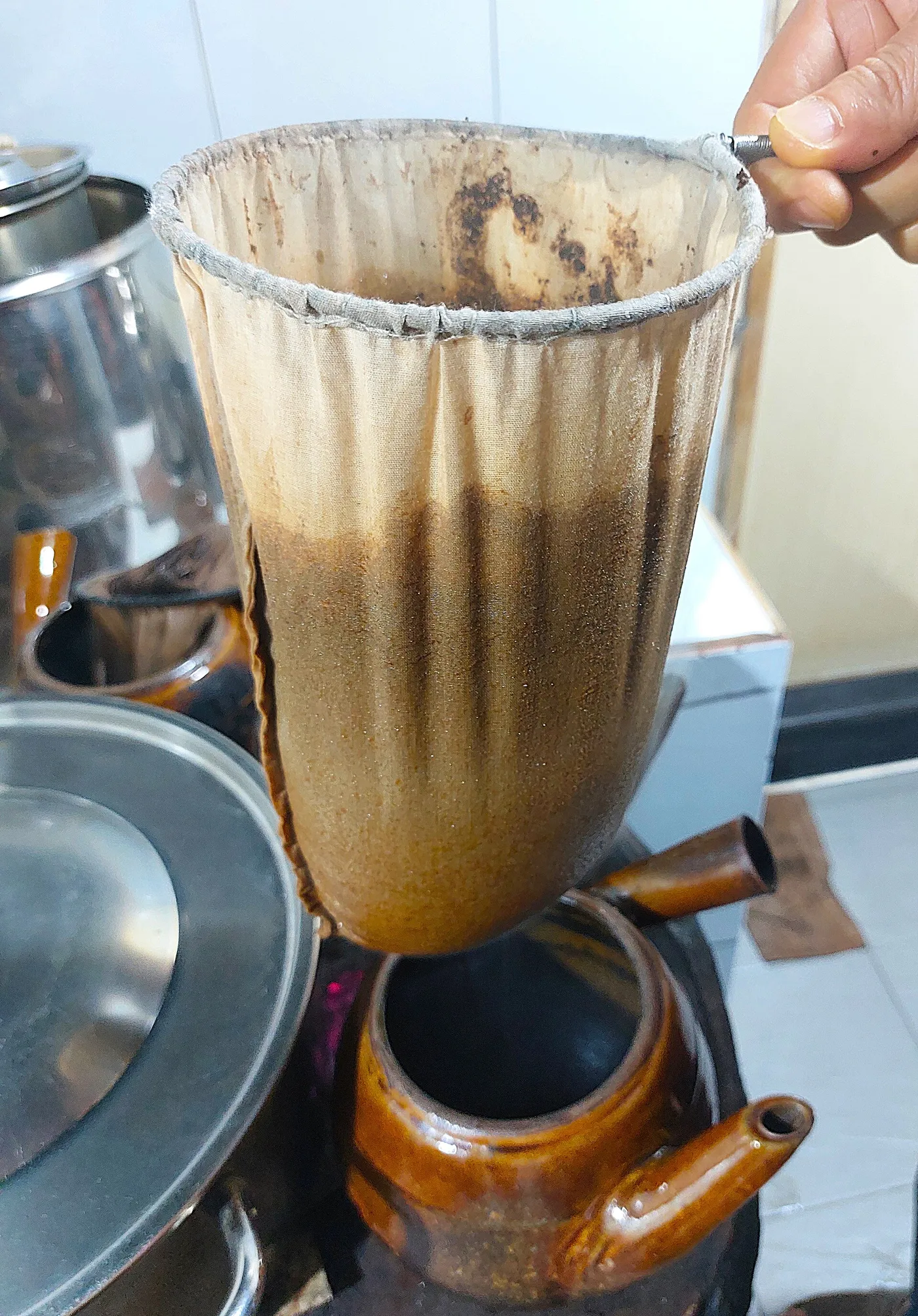 Cloth filter dripping coffee over a small brown ceramic pot