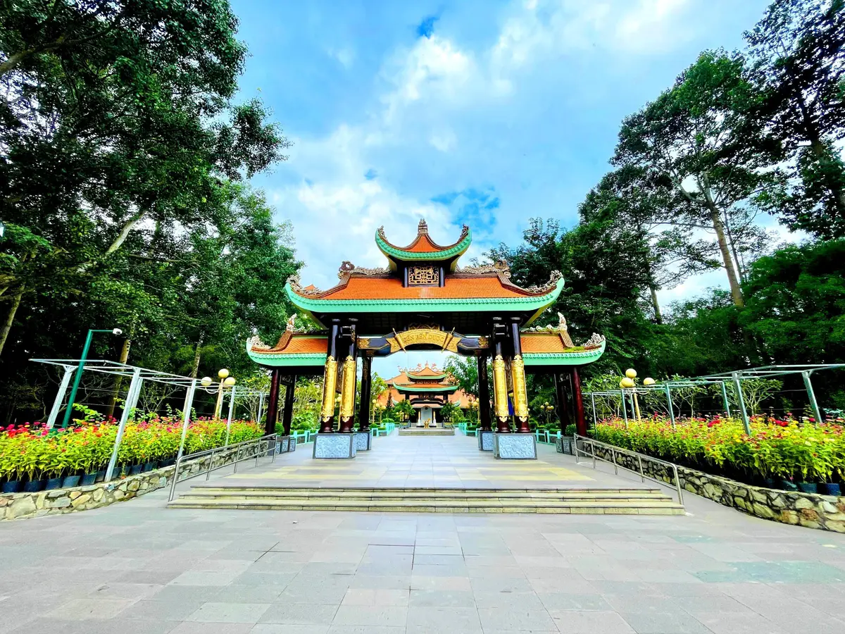 Memorial gate with tiered orange roofs behind flower beds and a paved plaza