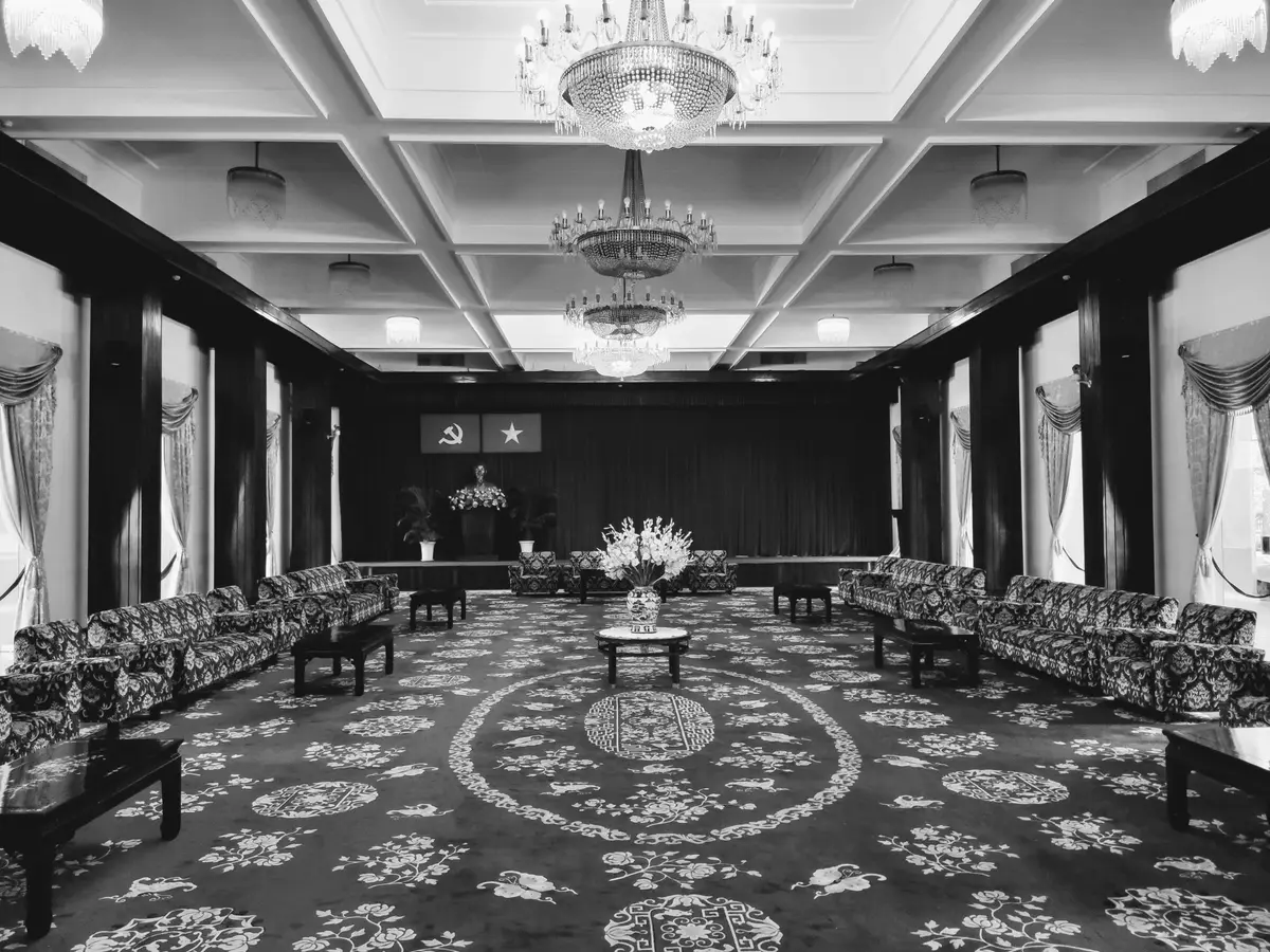 Black and white photo of a reception hall with patterned carpet, sofas and chandeliers