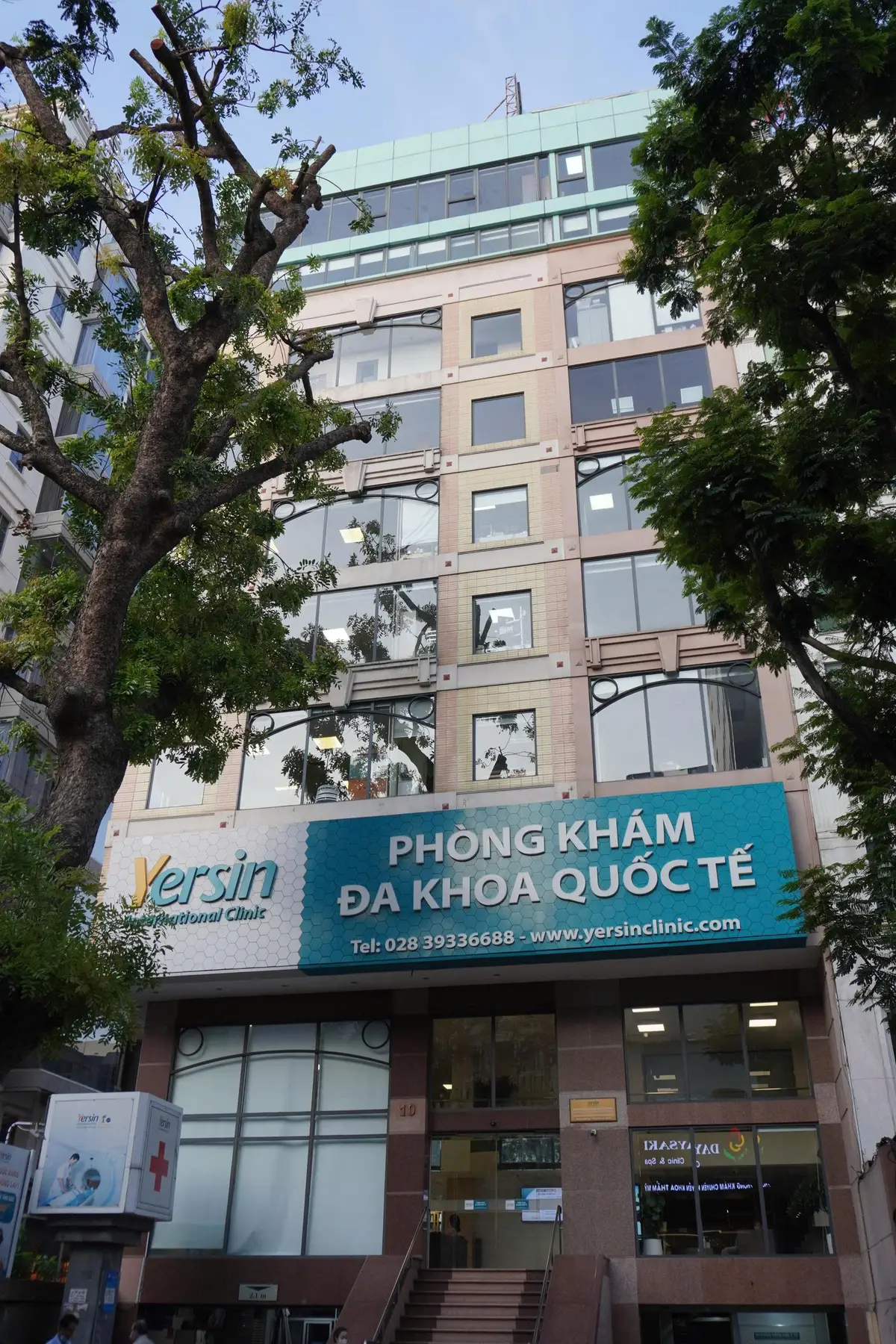 Yersin International Clinic street front with a teal sign above a glass-fronted building.