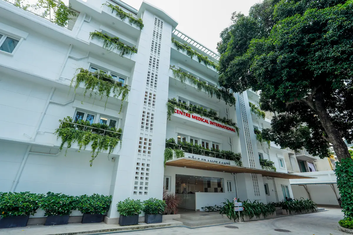 White five-storey clinic building with plants on the balconies and the clinic name above the entrance.