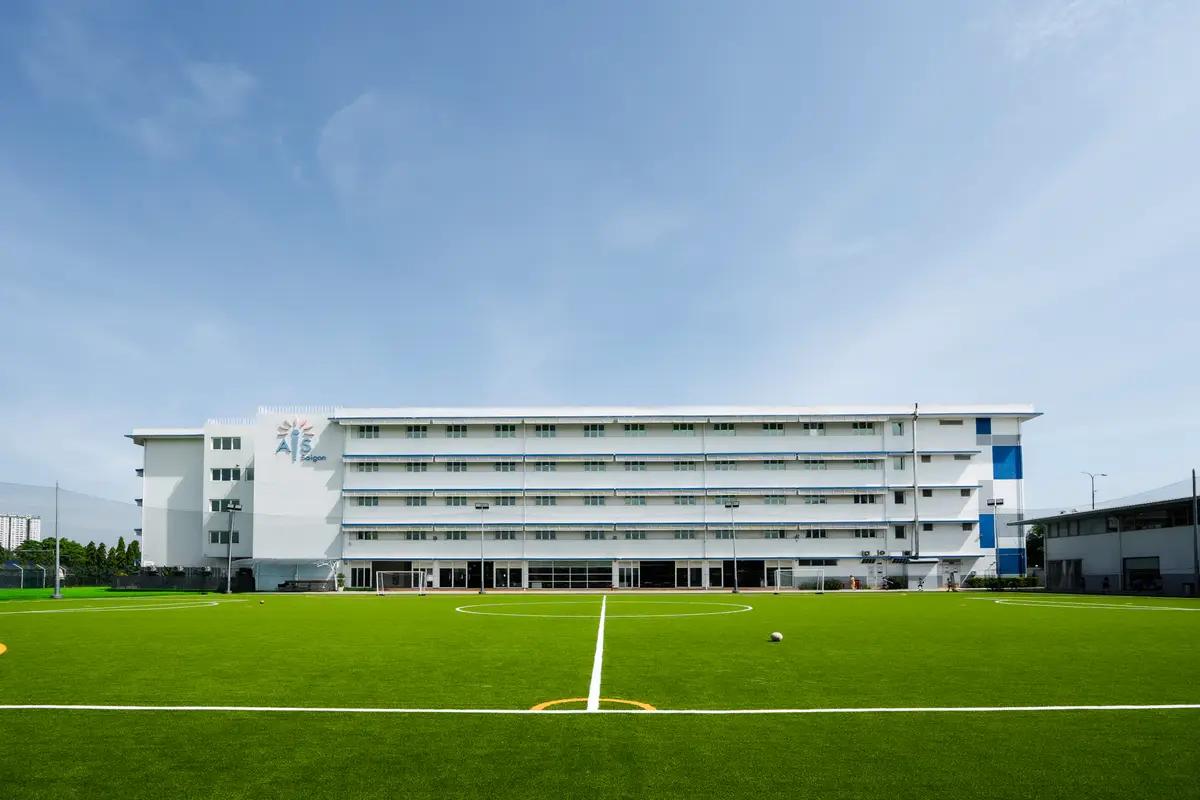 White multi-storey school block beside a green football pitch