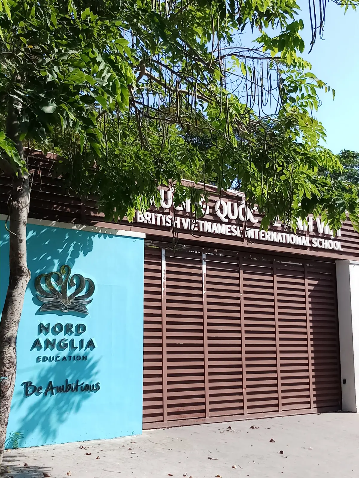 Brown louvred school entrance with a teal panel and the school name on a sign above