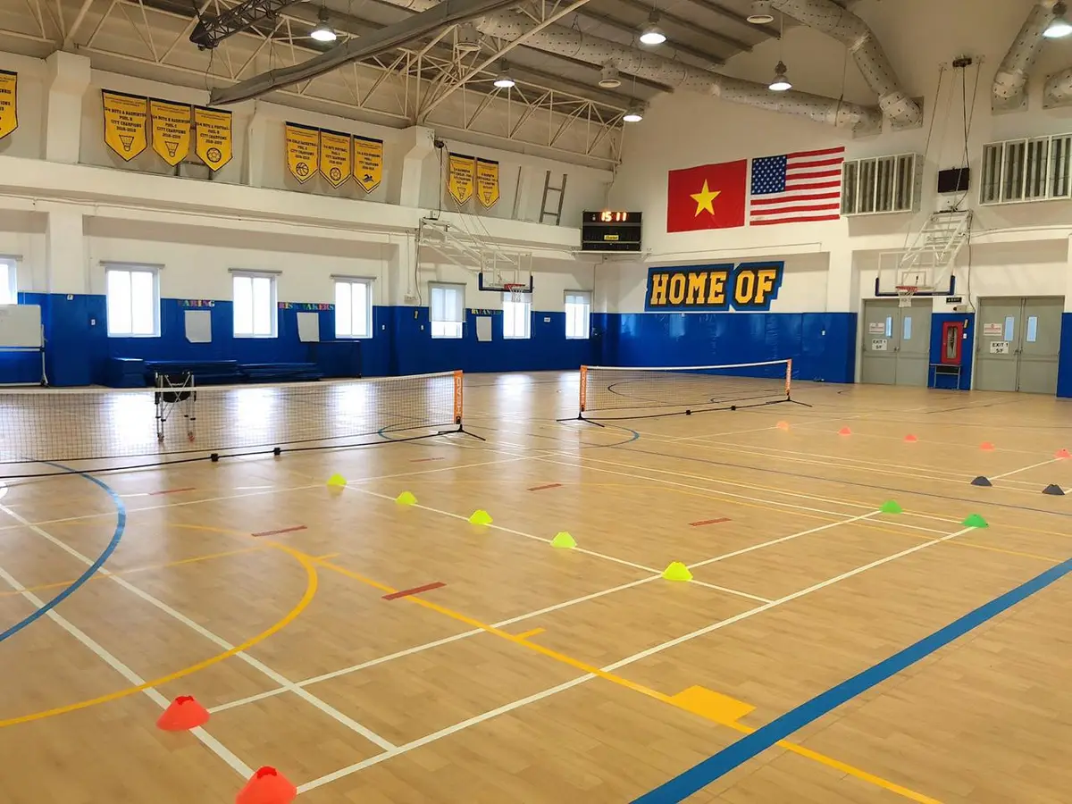 Indoor sports hall with a tennis net and coloured cones laid out on a wooden floor