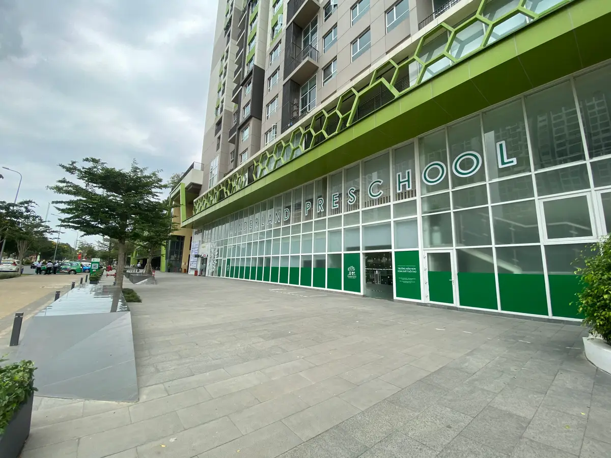 Glass-fronted ground floor of an apartment tower with a green band and school lettering beside a paved walkway