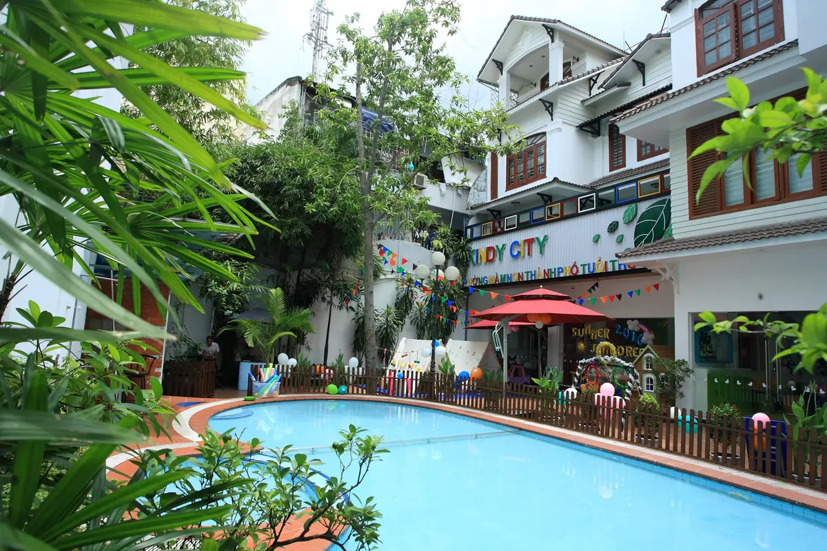 White building with green trim and a swimming pool and red parasol in the garden