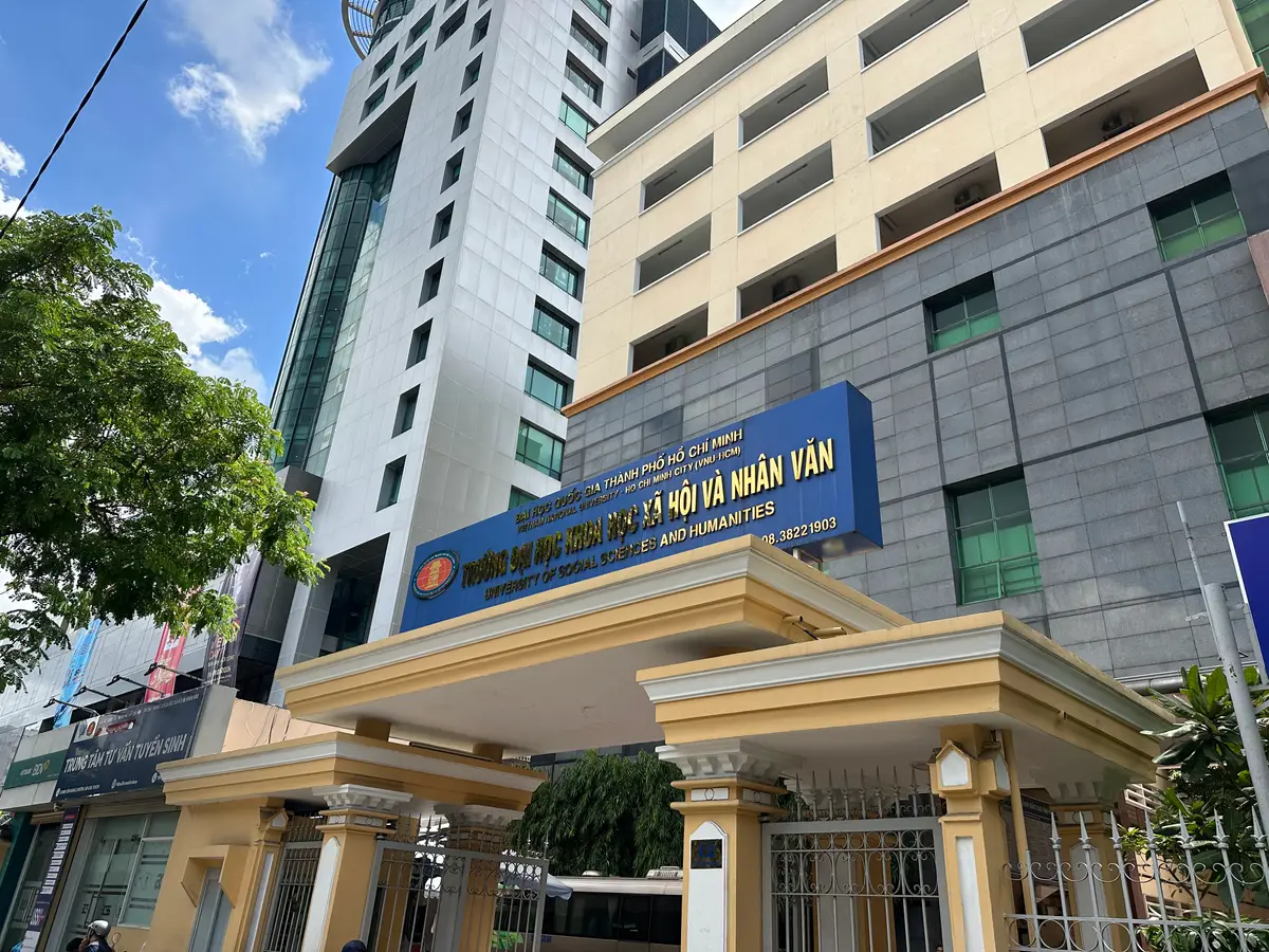 University entrance with a gold canopy and a blue name sign beside tall office buildings