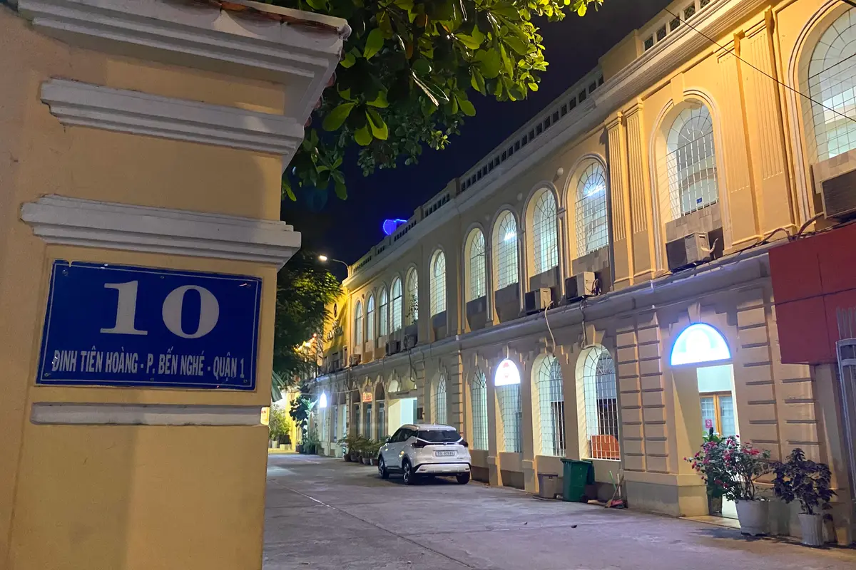 Yellow colonnaded building lit at dusk behind a blue street number plate