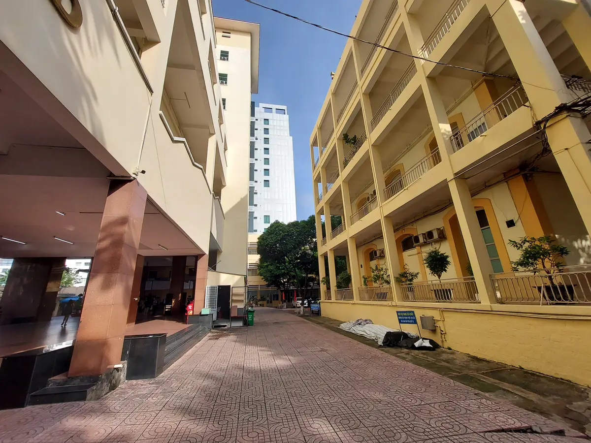 Yellow multi-storey classroom block with open balconies beside a brick courtyard