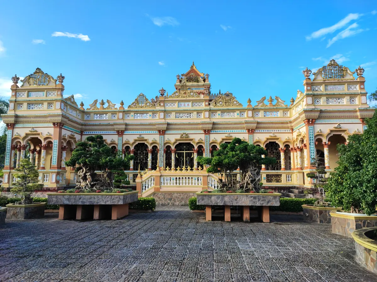 Yellow and cream pagoda hall with carved roofs, arches and trimmed trees in the courtyard