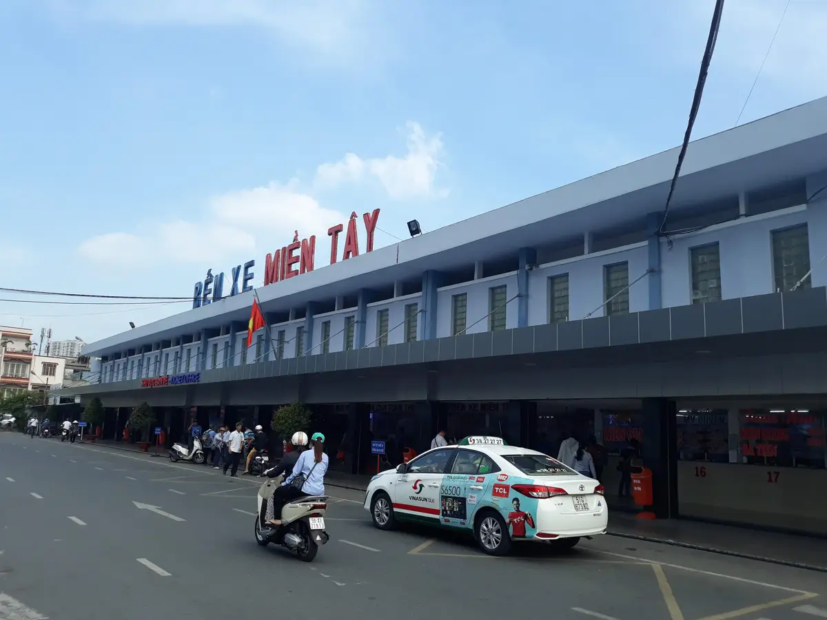 Long two-storey building with the sign Ben Xe Mien Tay and a white taxi in front
