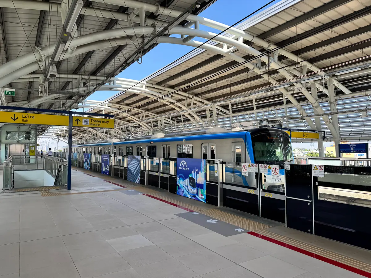 Blue and white train waiting at an open elevated platform with a curved steel roof