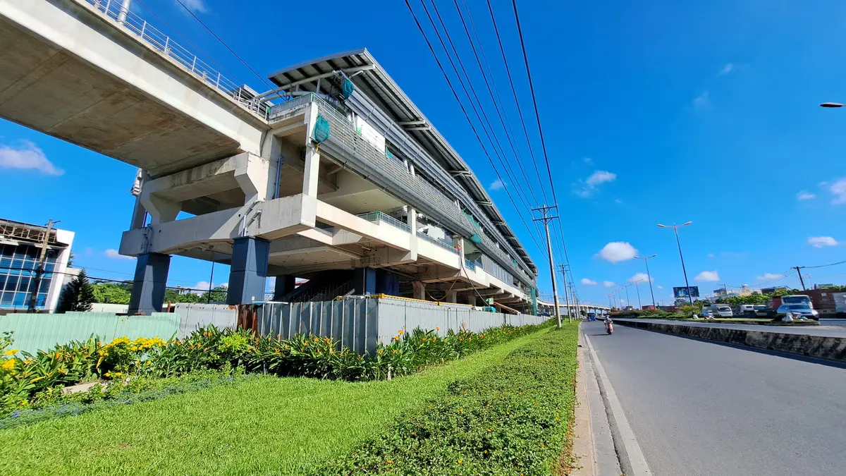 Elevated metro viaduct and station building beside a wide road under a blue sky