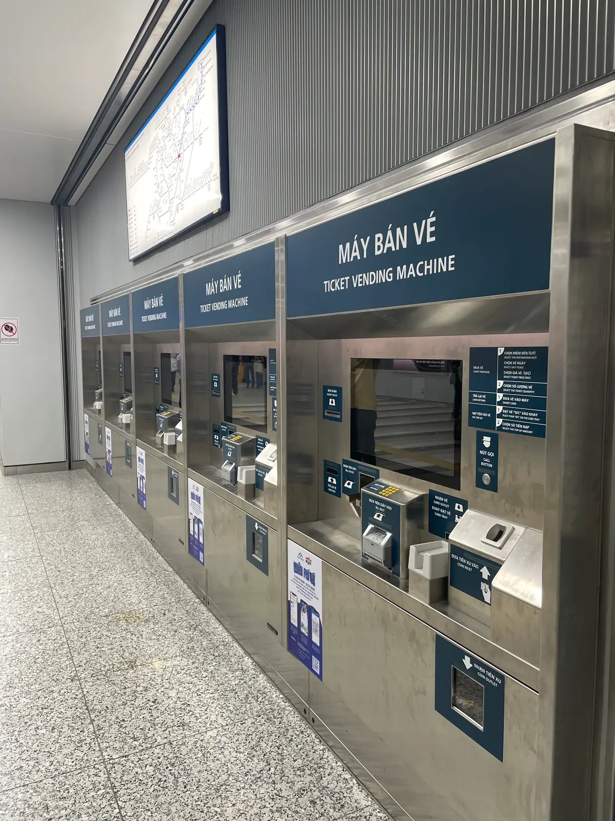 Row of steel ticket vending machines with screens and card slots in a station hall