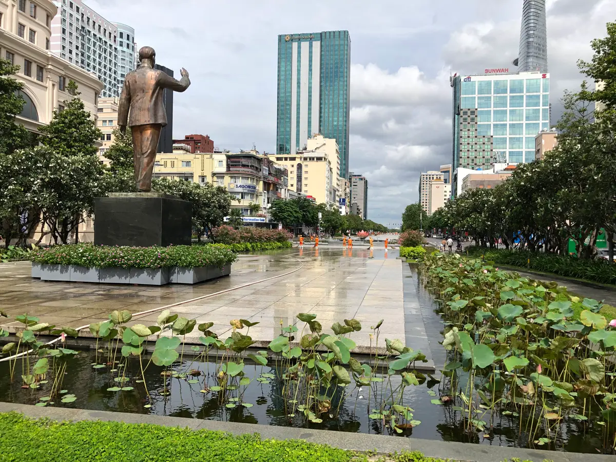 Wide paved boulevard with a statue, a lotus pond in the foreground and glass towers behind