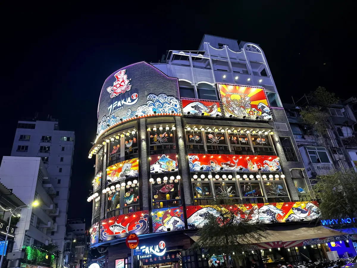 Curved multi-storey bar building covered in bright signs at night