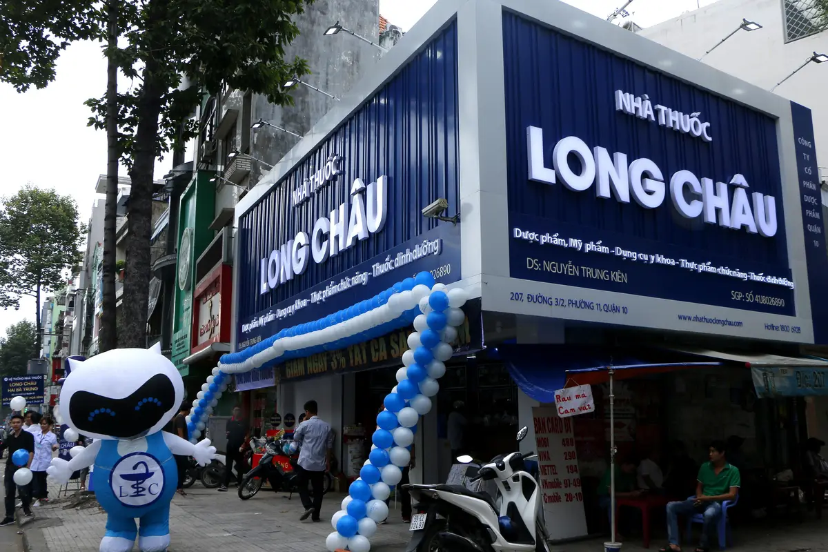 Blue Long Chau pharmacy sign above a street shopfront with a robot mascot and balloons.