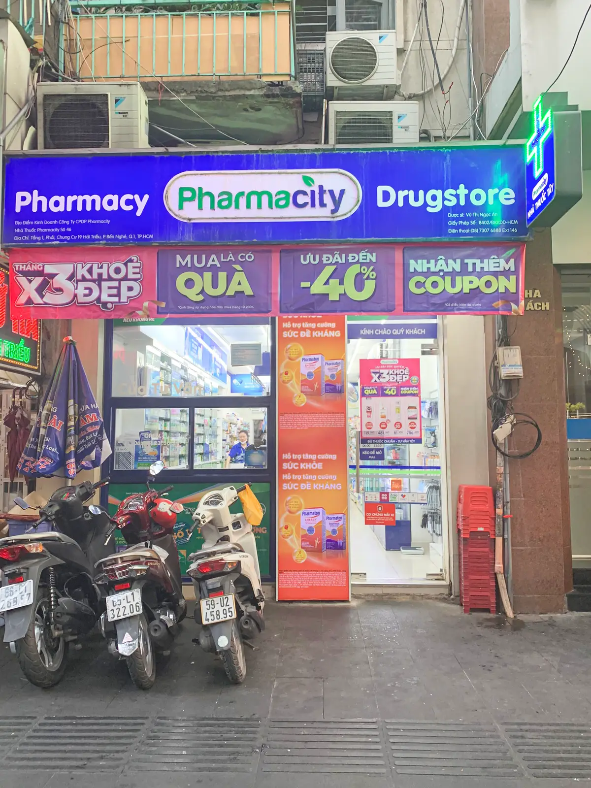 Pharmacity shopfront with promotional banners above the glass door and motorbikes parked outside.