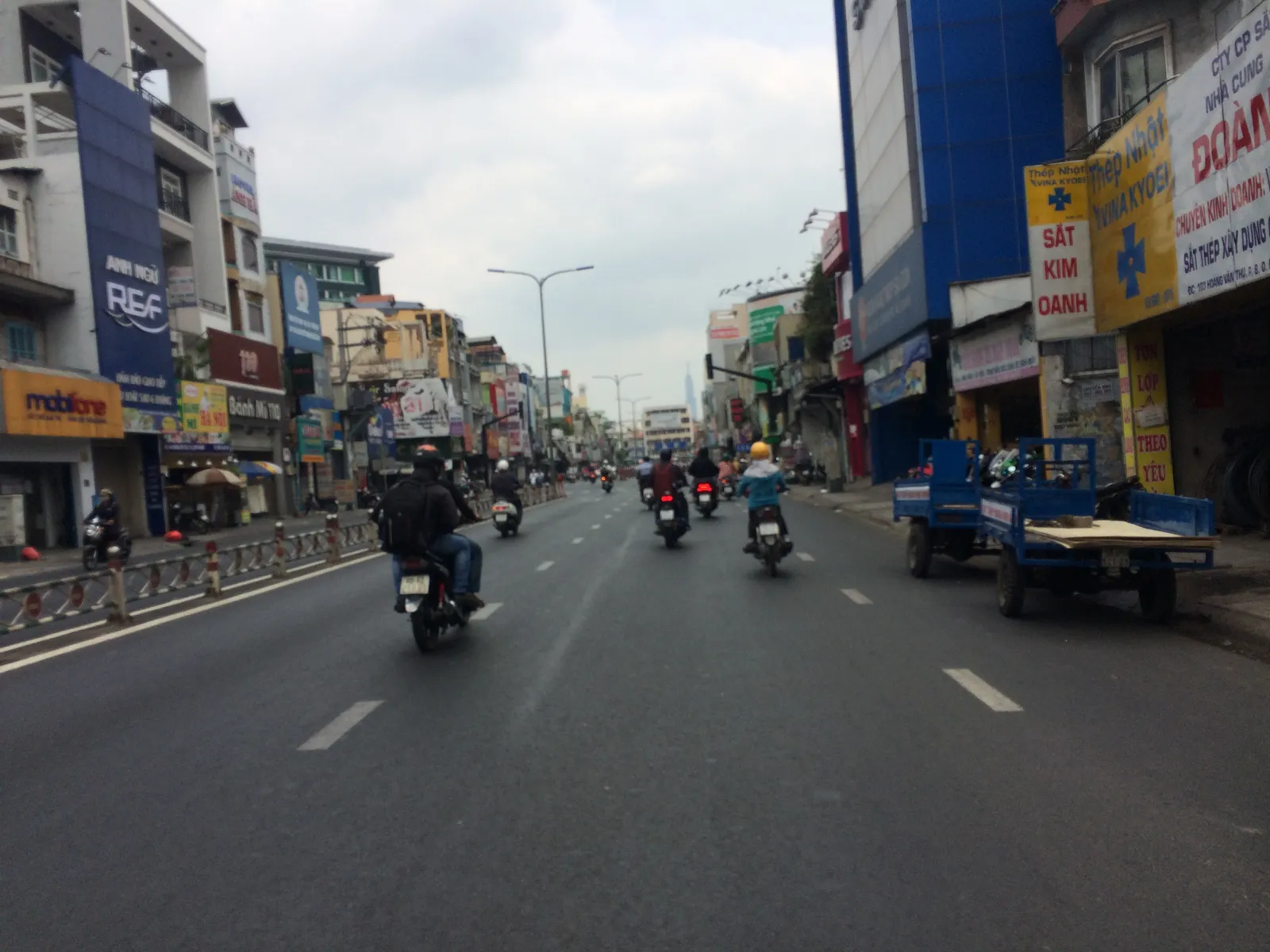 Wide street with motorbikes and shopfronts under a grey sky