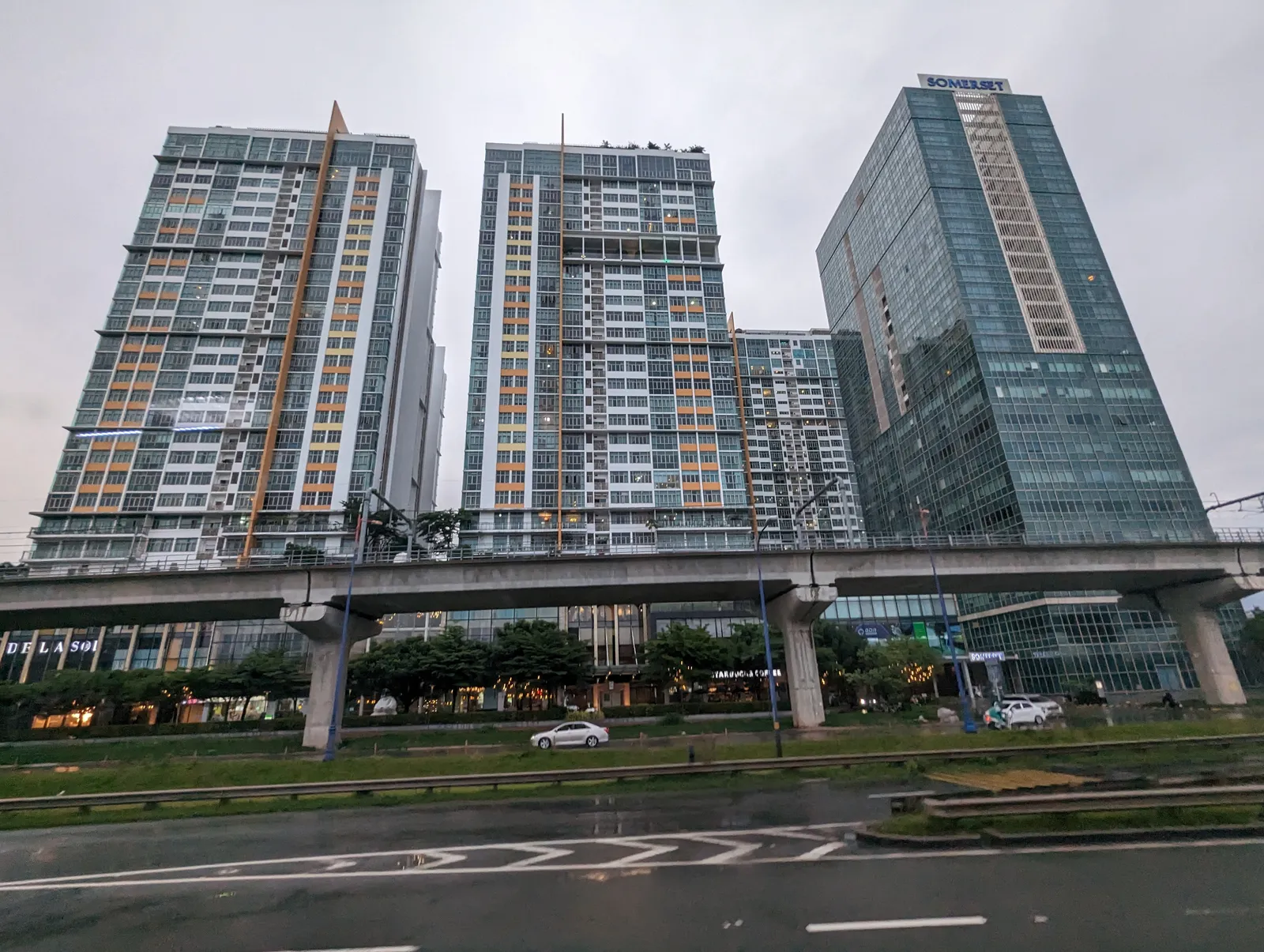 Apartment towers above a wet multi-lane road under a grey sky