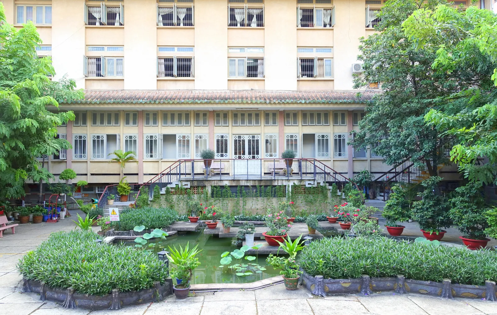 Inner garden courtyard with a lily pond, clipped shrubs and a yellow colonial-style building behind