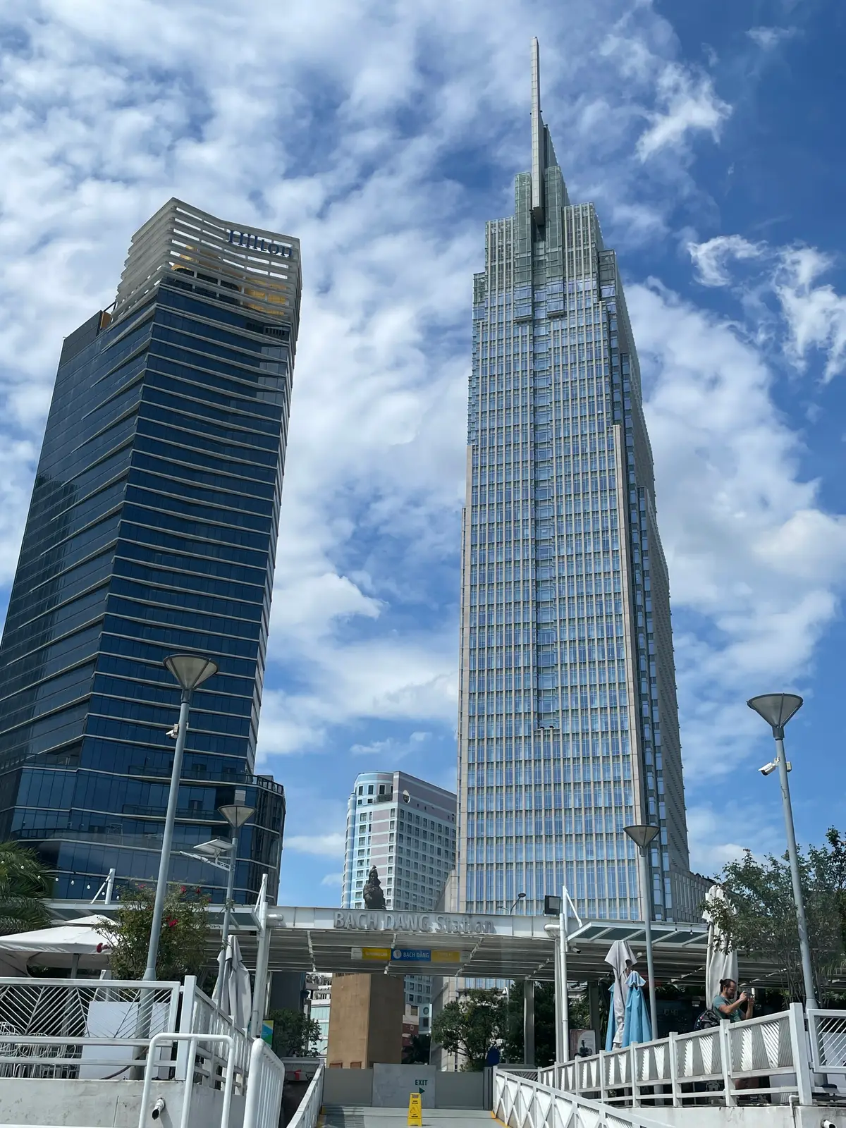 Two glass office towers rising side by side against a blue sky with a street lamp in front