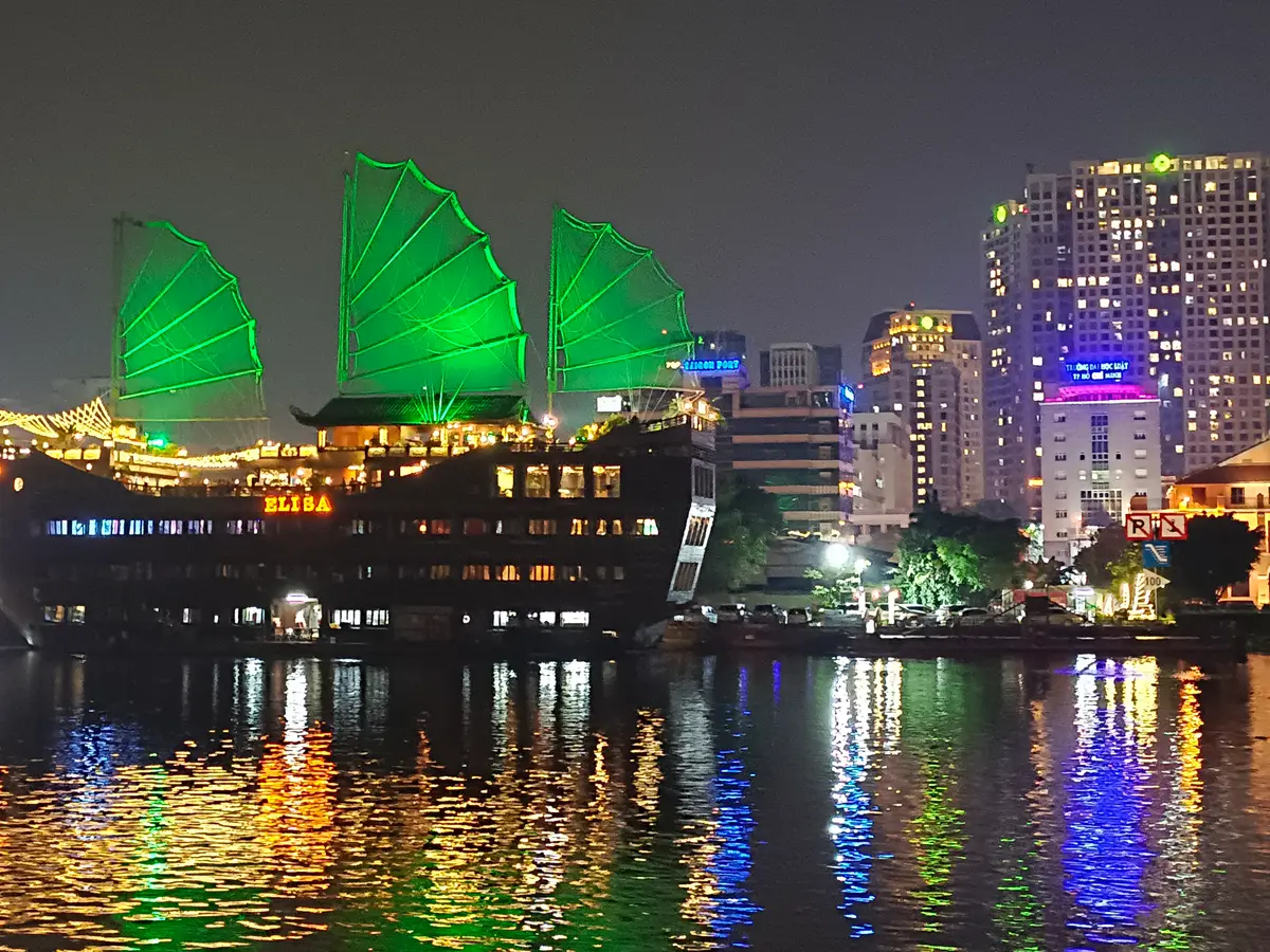 Junk-style boat with green sails lit at night, reflected in the river